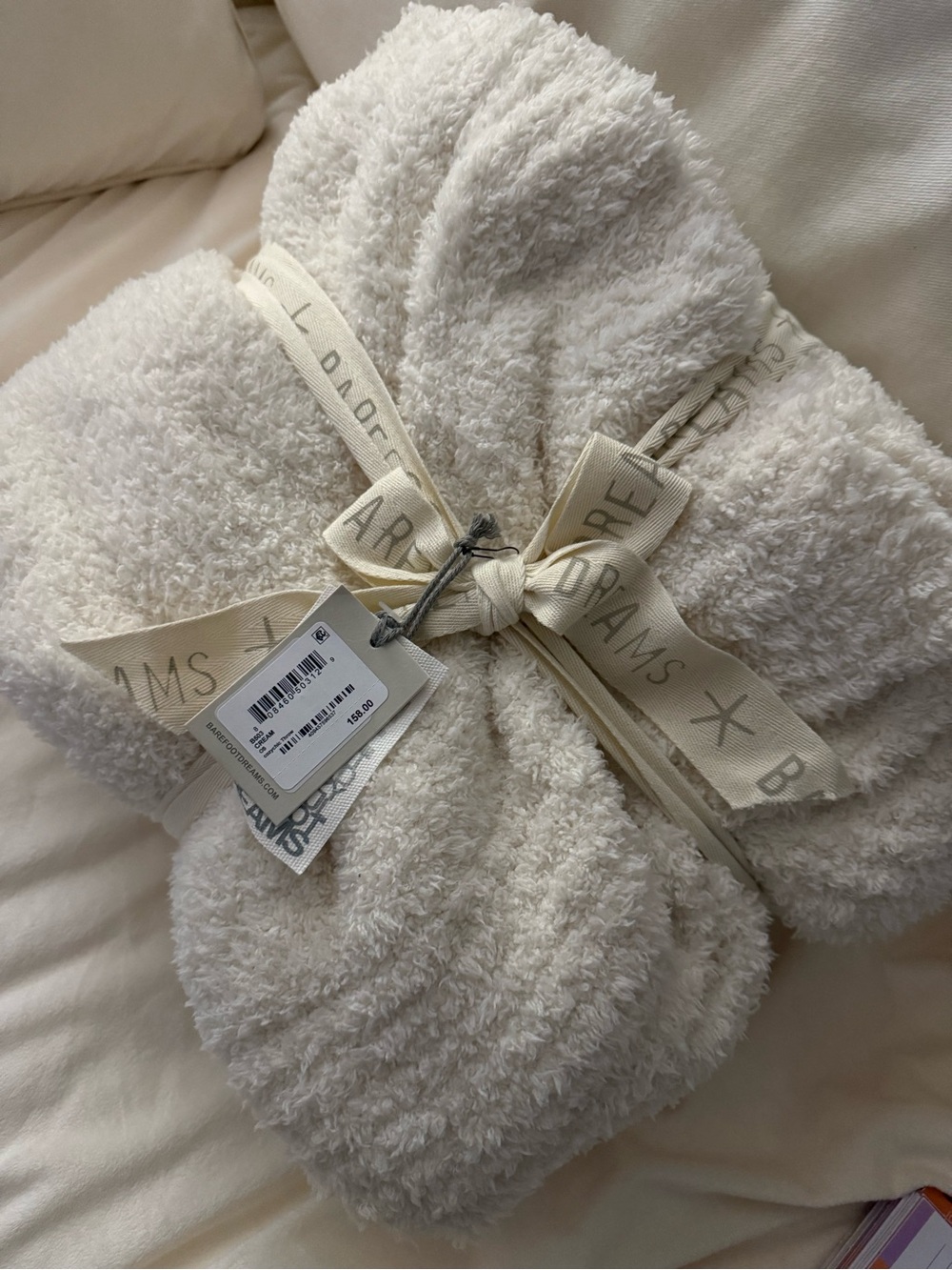 Barefoot Dreams plush cream throw with branded ribbon